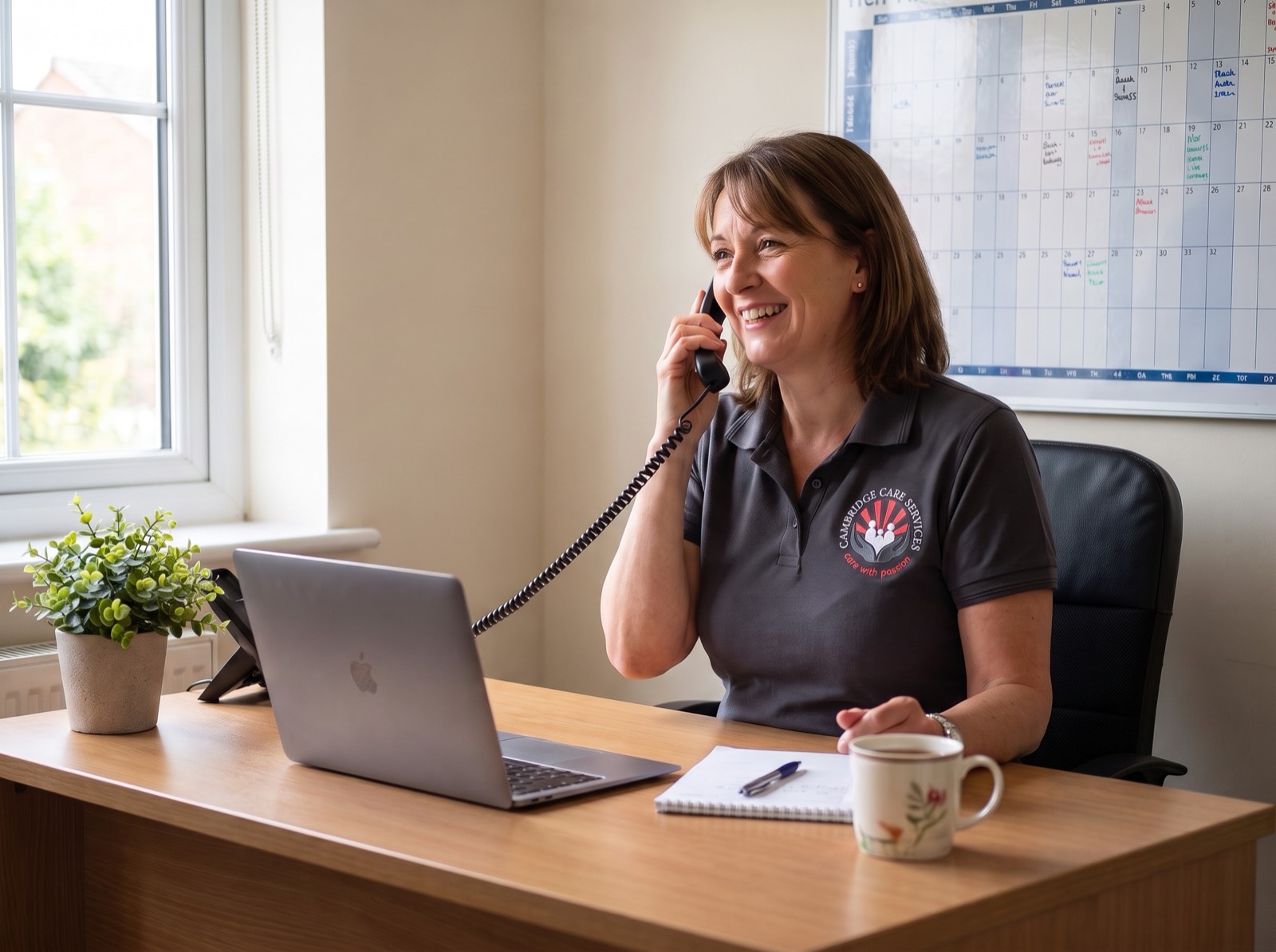 Cambridge Care Services coordinator in branded charcoal grey uniform taking a care enquiry call at the Sawston office