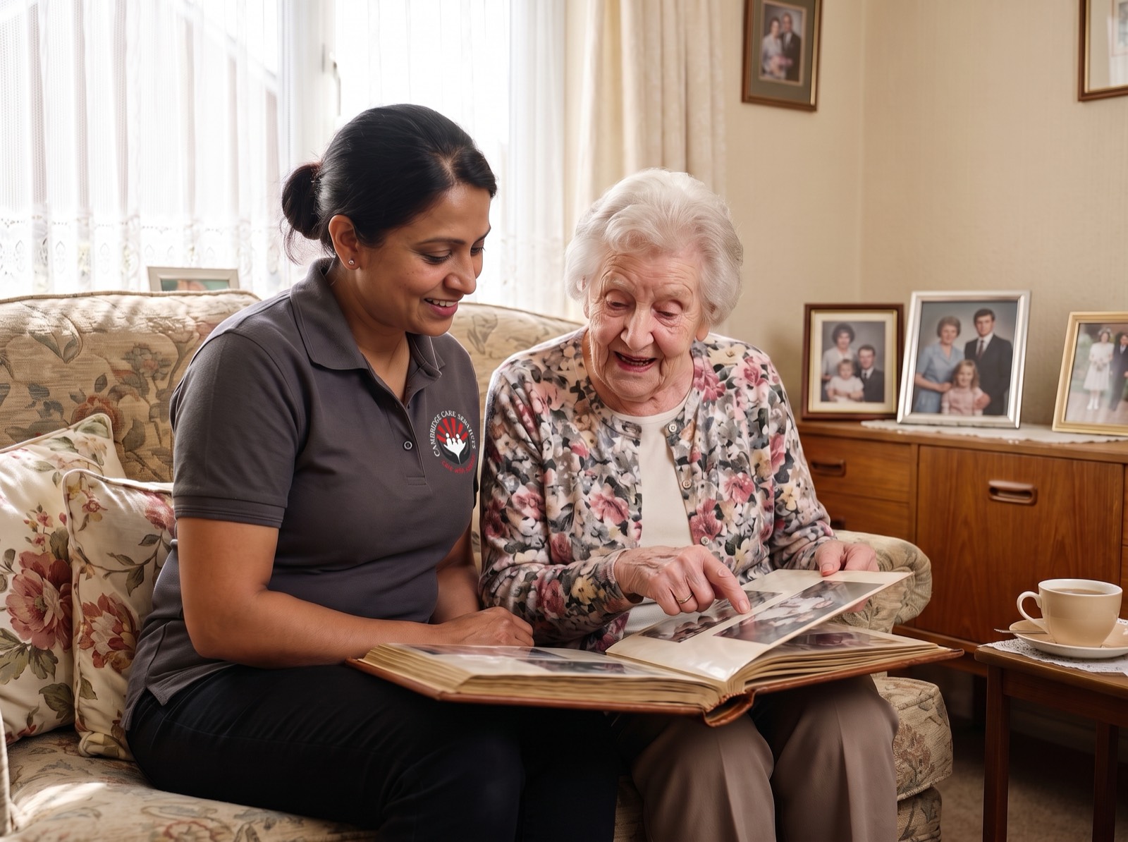 Cambridge Care Services dementia carer in branded charcoal grey uniform looking through a photograph album with an elderly woman at home in Cambridge