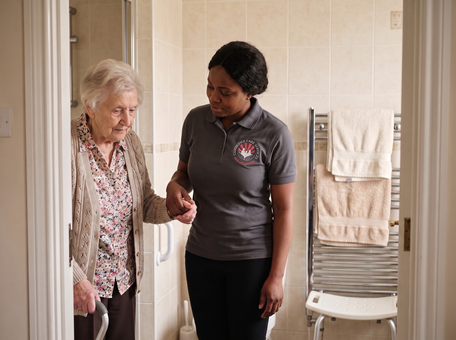 Cambridge Care Services carer in branded charcoal grey uniform supporting an elderly woman safely at the bathroom door in Cambridge